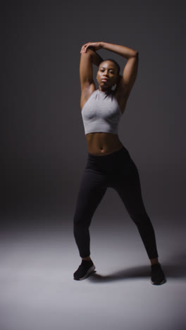 Vertical-Video-Studio-Shot-Of-Young-Woman-Wearing-Gym-Fitness-Clothing-Warming-Up-For-Exercise